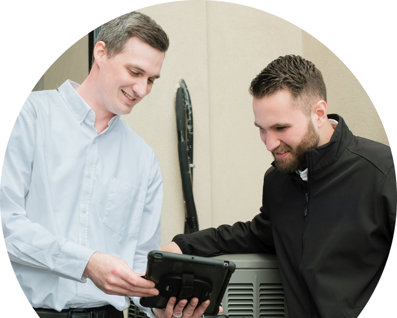 A Wardlaw technician in a white shirt shows service details on a tablet to a smiling client in a black jacket, standing beside an AC unit outside a beige building. A Wardlaw technician in a white shirt shows service details on a tablet to a smiling client in a black jacket, standing beside an AC unit outside a beige building.