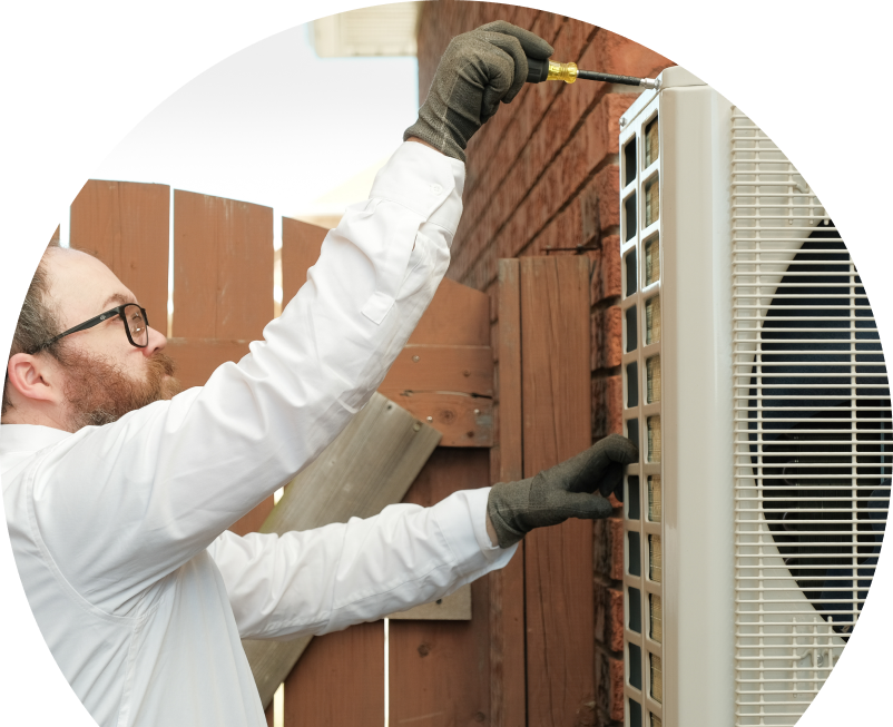 Wardlaw service personnel working on an AC condenser, using a screwdriver to secure the unit’s panel outdoors beside a wooden fence. Wardlaw service personnel working on an AC condenser, using a screwdriver to secure the unit's panel outdoors beside a wooden fence.