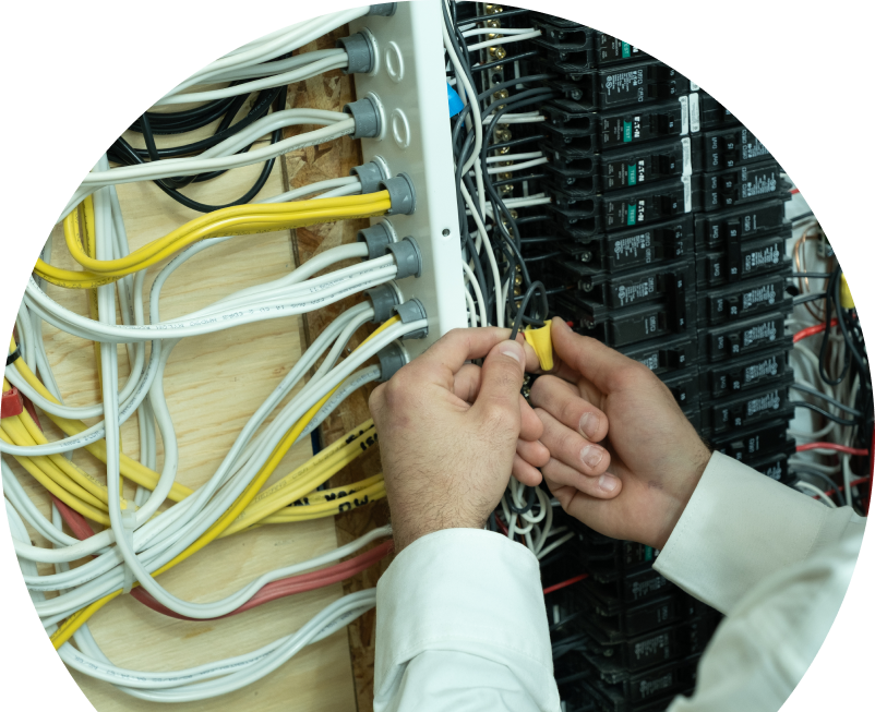 Wardlaw service personnel working on electrical installations, connecting wires inside a residential breaker panel with neatly arranged colored cables on a plywood backing. Wardlaw service personnel working on electrical installations, connecting wires inside a residential breaker panel with neatly arranged colored cables on a plywood backing.