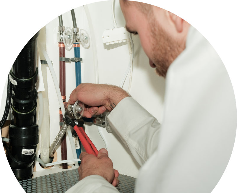 Wardlaw plumbing expert tightening connections under a sink during a faucet installation, surrounded by hot and cold water supply lines and PVC drainage. Wardlaw plumbing expert tightening connections under a sink during a faucet installation, surrounded by hot and cold water supply lines and PVC drainage.