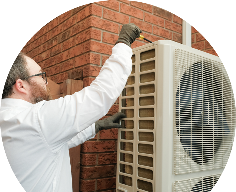 Wardlaw HVAC specialist using a screwdriver to complete a heat pump installation beside a brick wall. Wardlaw HVAC specialist using a screwdriver to complete a heat pump installation beside a brick wall.