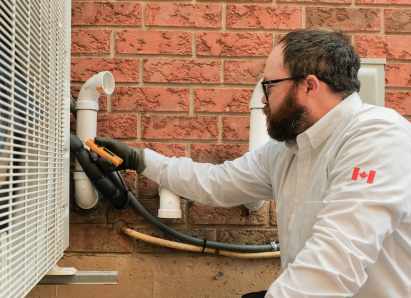 A Wardlaw HVAC specialist wearing glasses and gloves uses a diagnostic tool to service an outdoor AC unit beside a brick wall. A Wardlaw HVAC specialist wearing glasses and gloves uses a diagnostic tool to service an outdoor AC unit beside a brick wall.