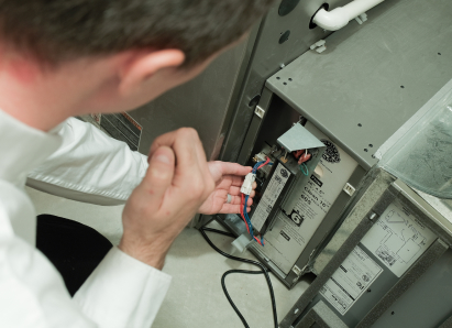 A Wardlaw heating technician inspecting internal wiring during a service check on a residential heating unit. A Wardlaw heating technician inspecting internal wiring during a service check on a residential heating unit.