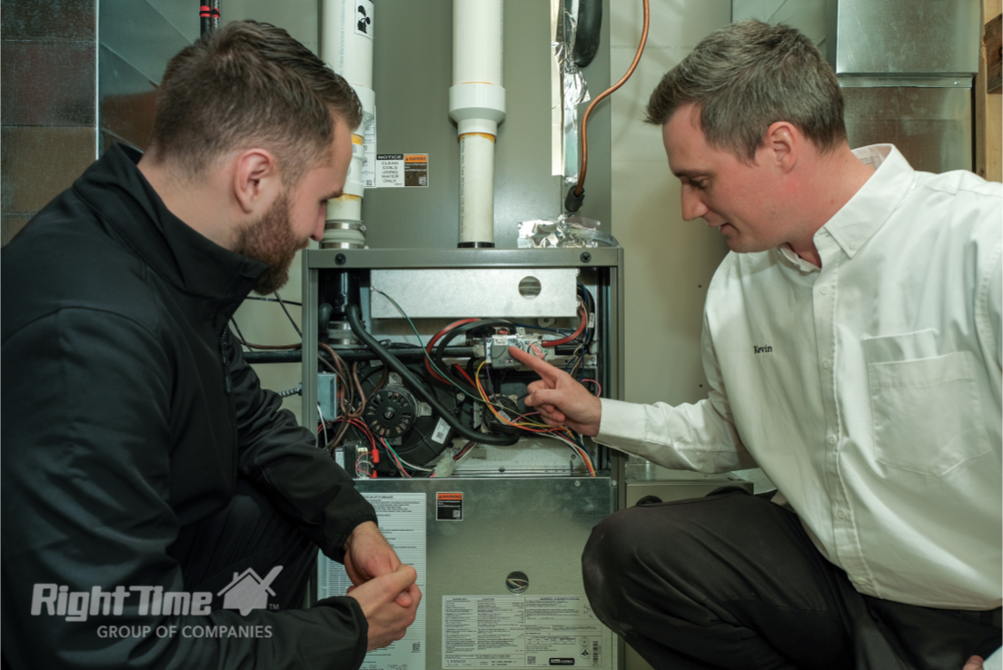 Two HVAC technicians in Sault Ste Marie inspecting a residential furnace system, examining why furnace filter stays clean with tools and diagnostic equipment visible